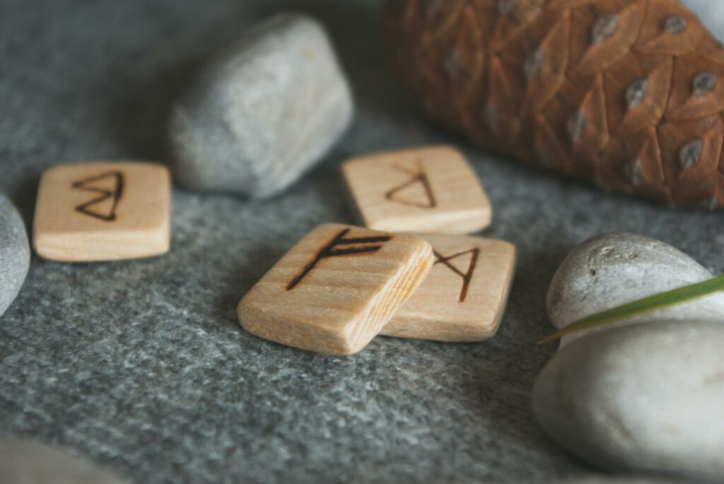 From above set of wooden runes and stones placed in knitted wool blanket near fir cone