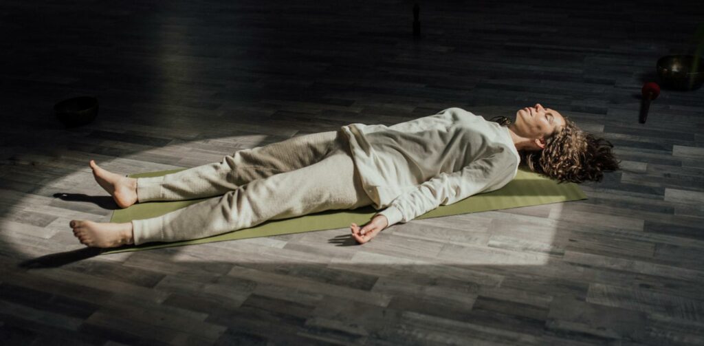 Woman lying on a yoga mat indoors, meditating and relaxing in a calm setting.
