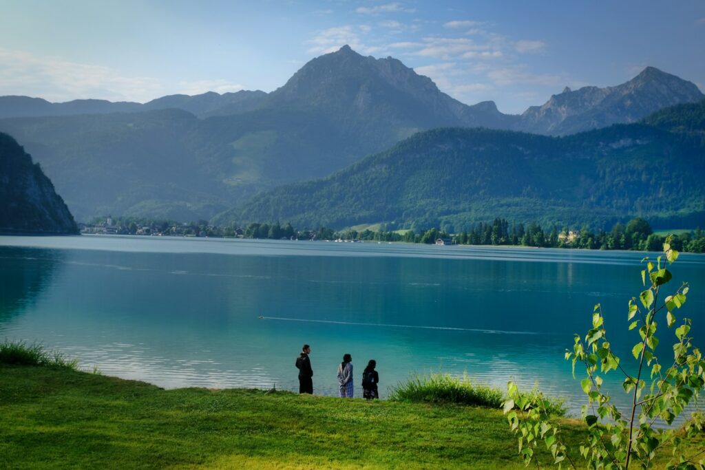People stand by a lake overlooking mountains.