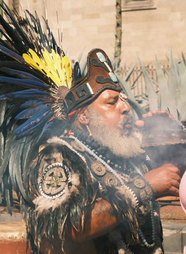 Man in traditional headdress blowing smoke from bowl